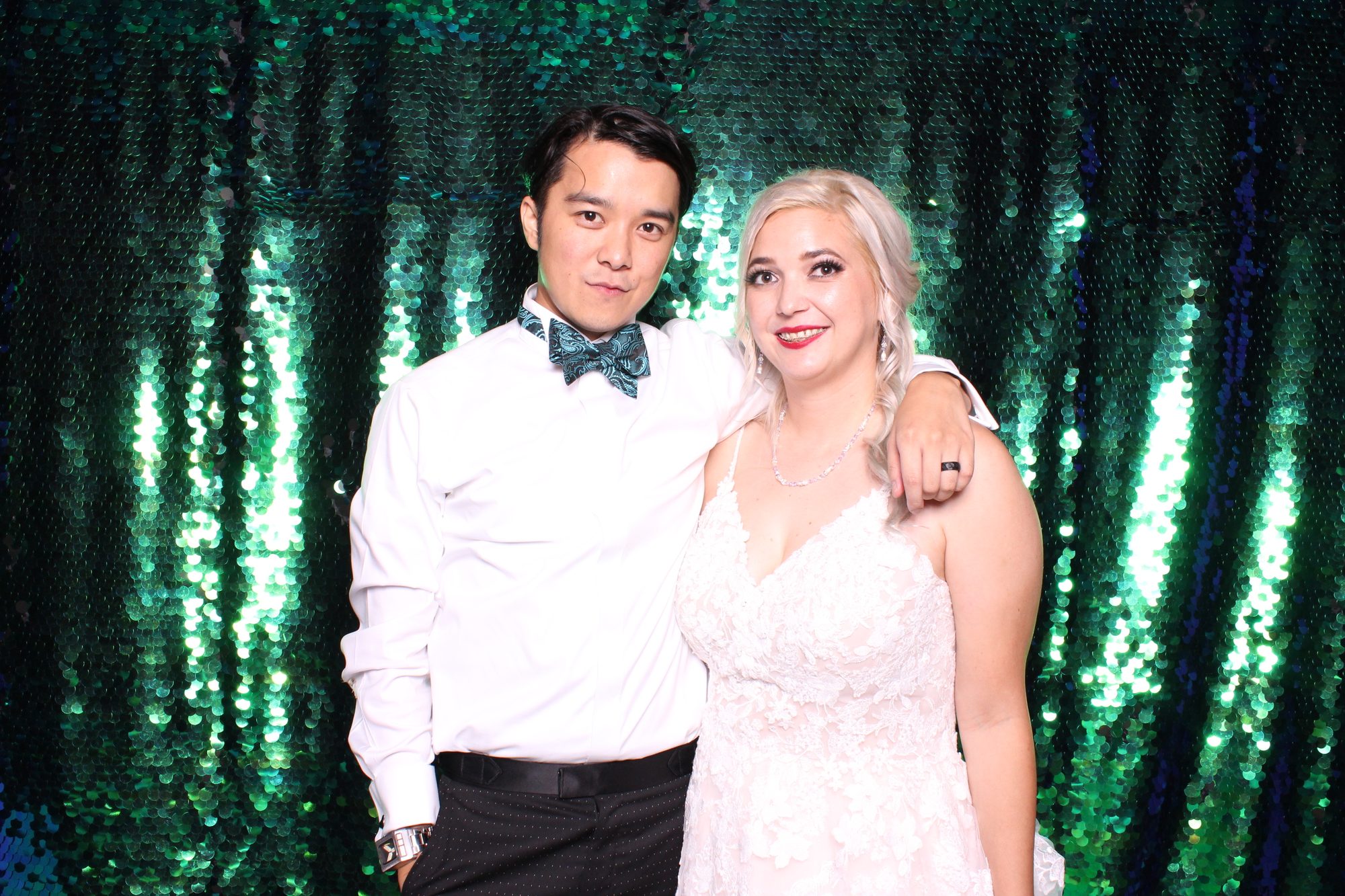 Wedding couple posing at photobooth with green sequin backdrop