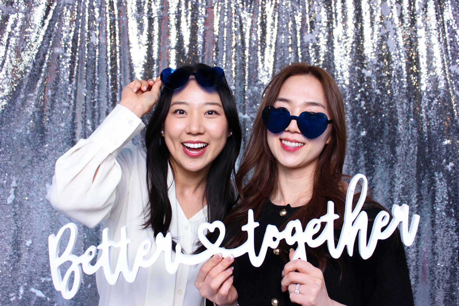 Guests posing with photobooth props and a custom sign in front of a silver sequin backdrop
