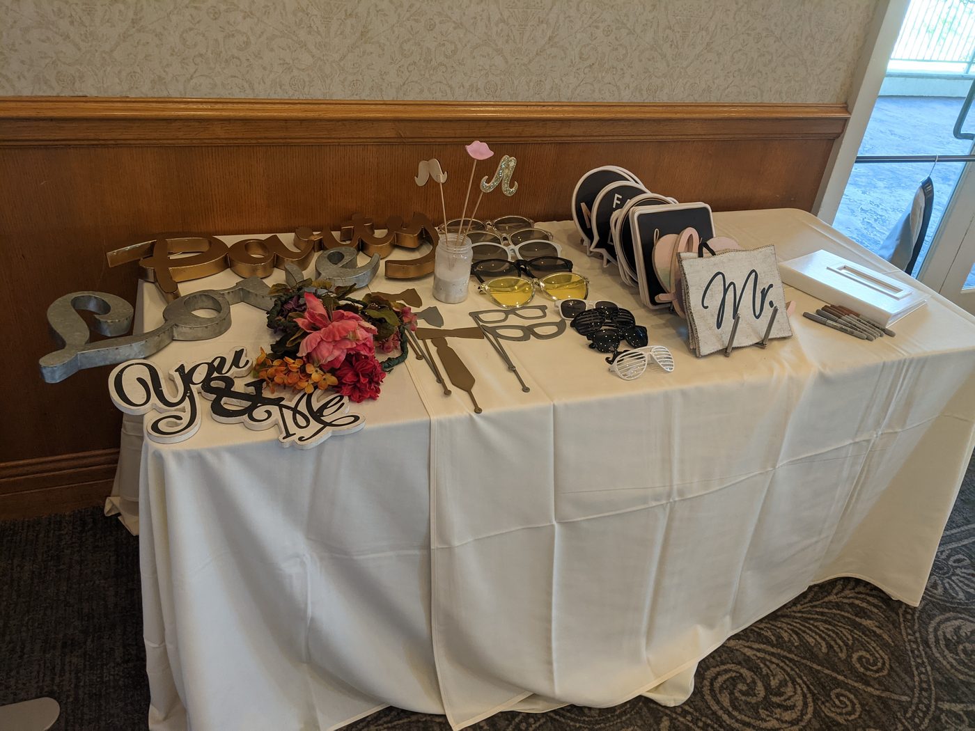 Photobooth prop table with 'Party Love' and 'You & Me' sign cutouts in a hotel ballroom