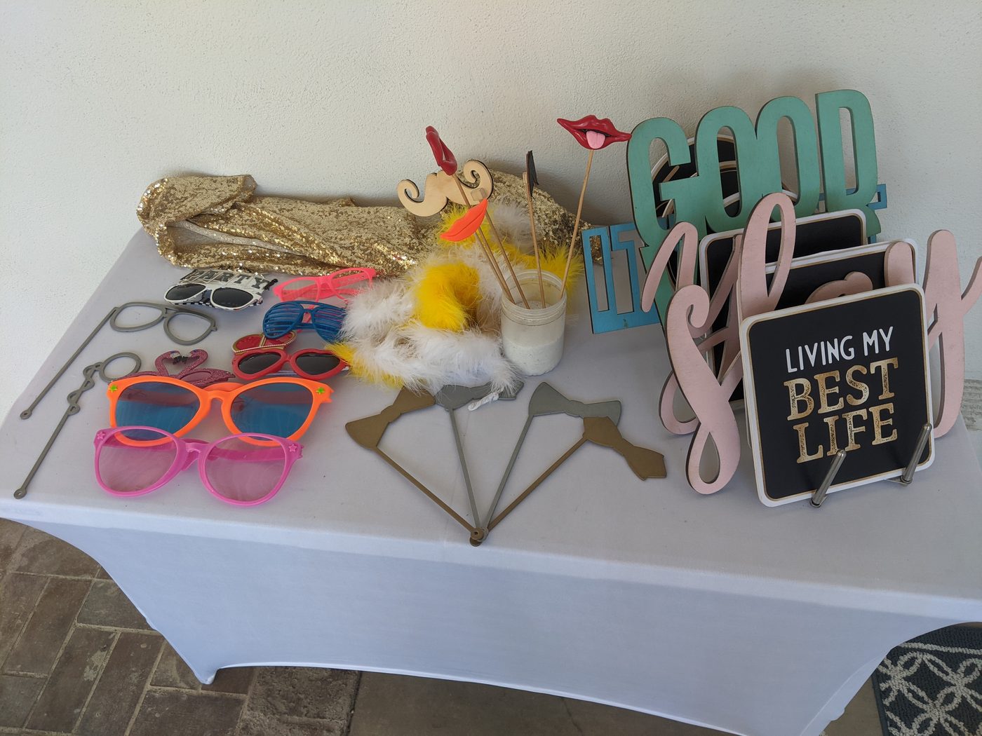 Photobooth prop table with sunglasses and a 'Living My Best Life' sign at an evening event