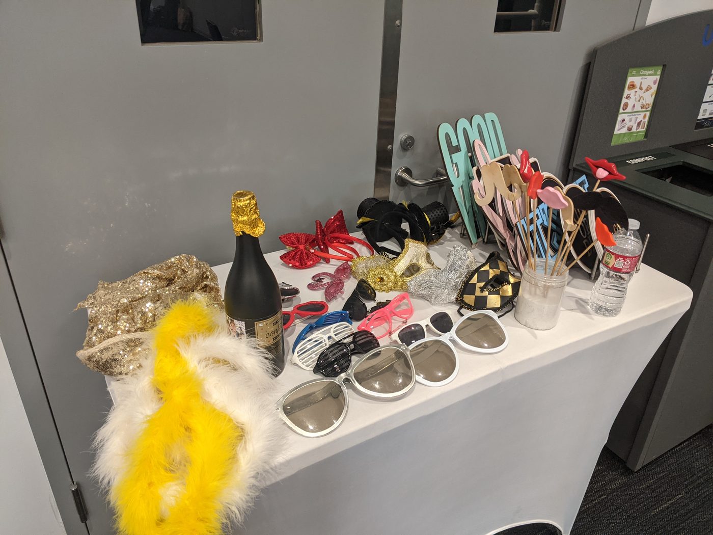 Photobooth prop table with champagne, a feather boa, and fun sign cutouts at an event