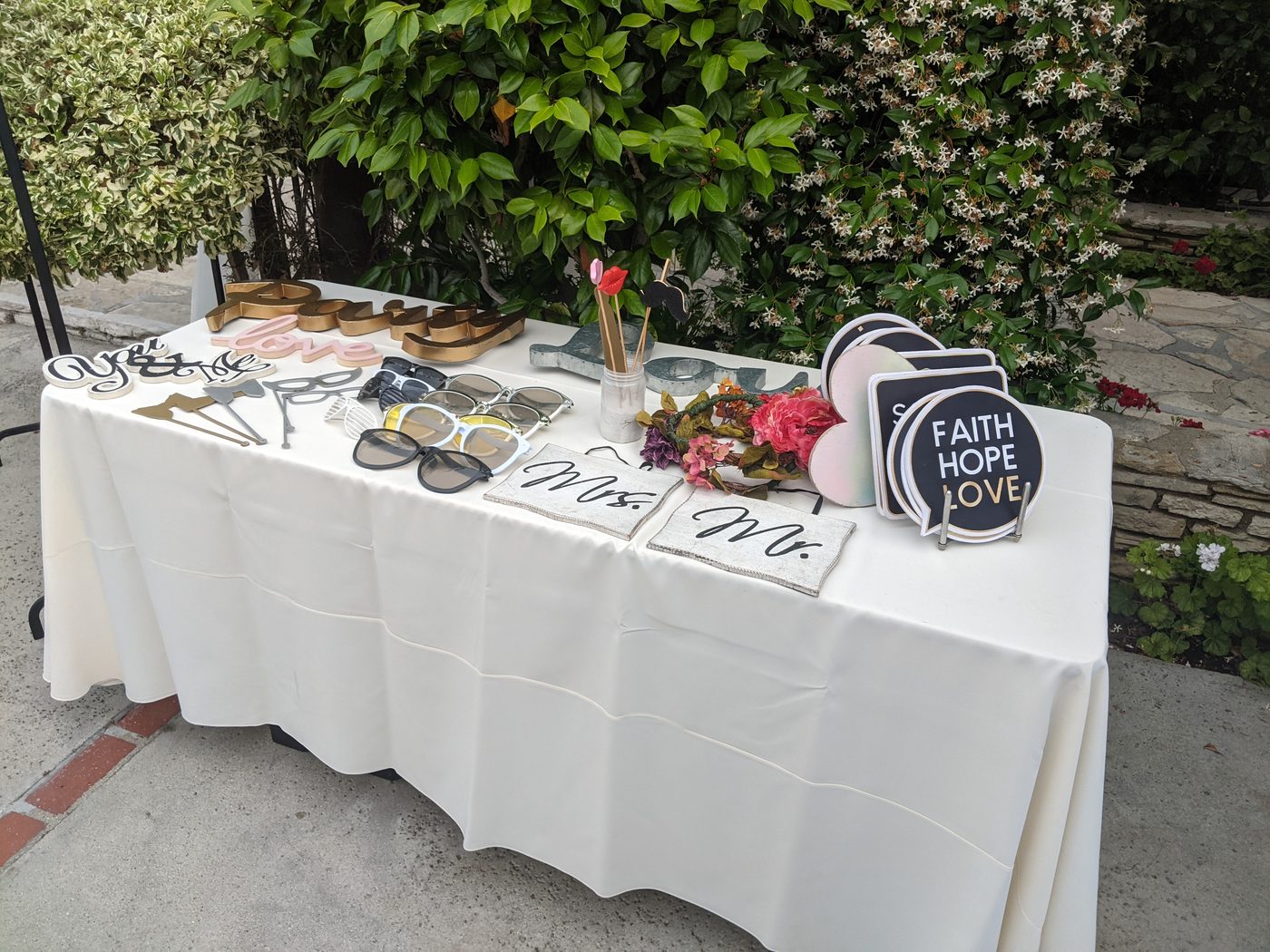 Photobooth prop table with a 'Faith Hope Love' heart sign and sunglasses at a garden wedding