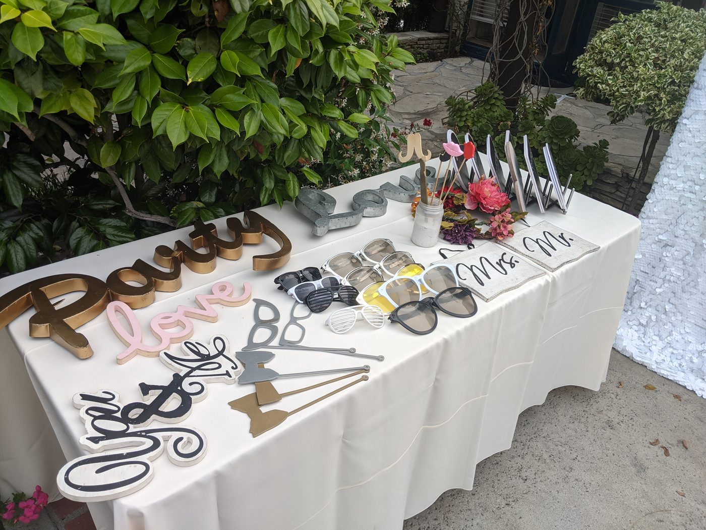Photobooth prop table with 'Party Love' and 'Yes To The Dress' wedding sign props in a garden