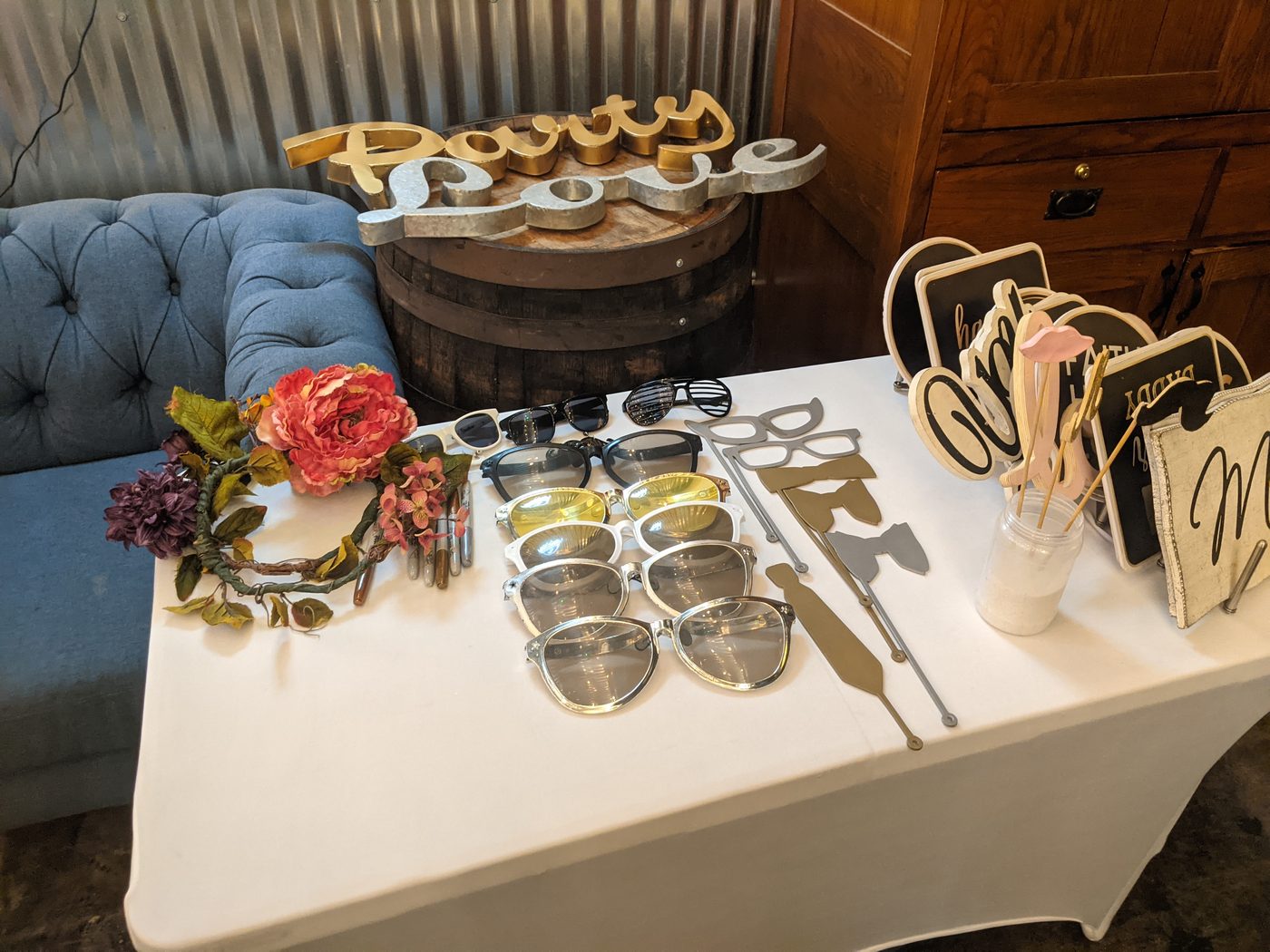 Photobooth prop table with 'Party Love' sign cutouts and a floral crown at a rustic barn venue