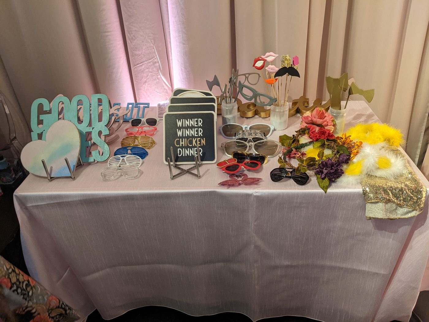 Photobooth prop table with a 'Winner Winner Chicken Dinner' sign and florals at an uplit reception